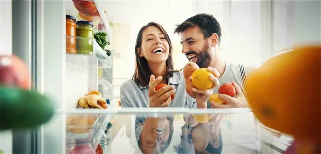 Casal olhando dentro da geladeira aberta