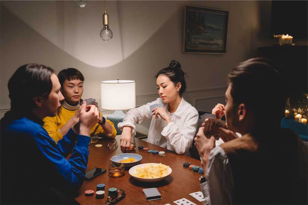 Pessoas jogando carta na mesa com prato de batata do lado
